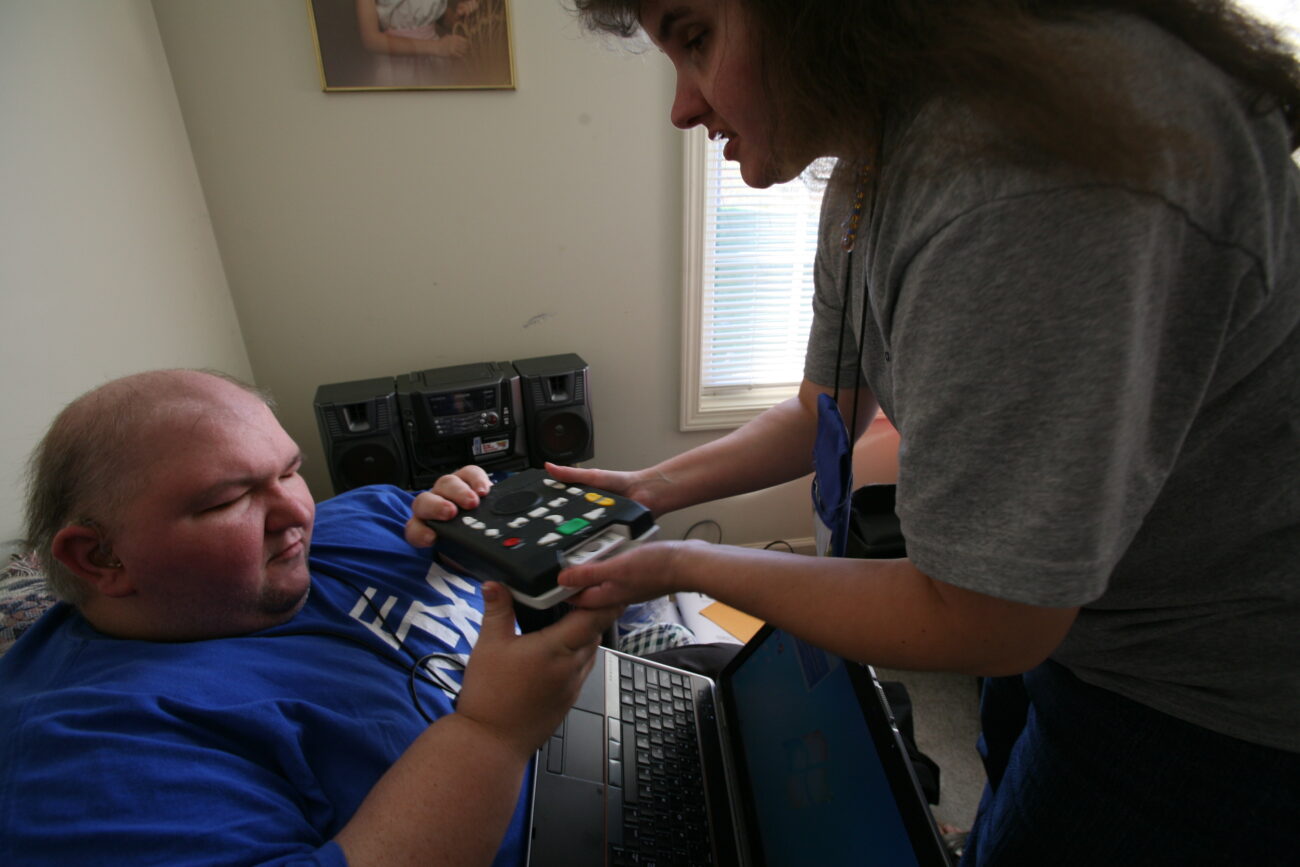 Paula hands Shannon a device to help them amplify sounds. Shannon's hearing has been declining for the past 3 years and they always joke that it's only Paula's voice he can hear clearly. Photo by Genevieve Adams