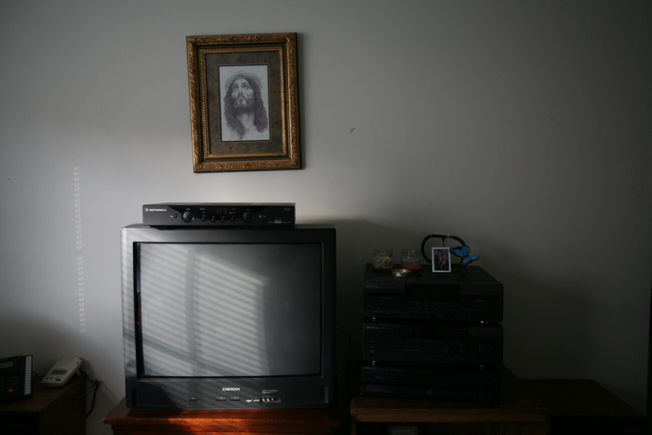 A crooked picture of Jesus, given to Paula by her spiritual leader after her mother passed, hangs over the TV. Photo by Genevieve Adams