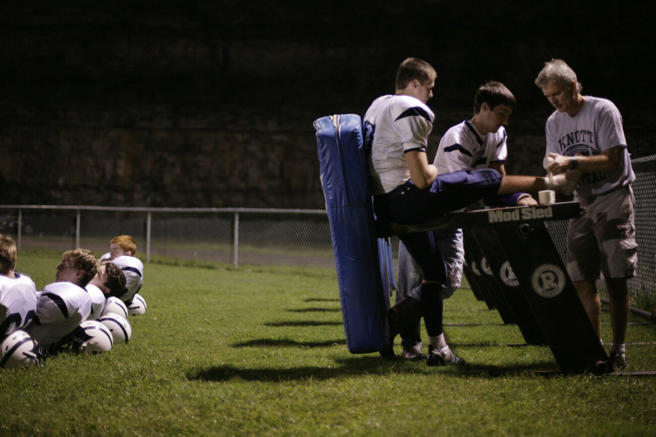 Using Seth Hall's arm cast as support, head coach Beder tapes a player's ankle during halftime of the Patriot's game against Pike County Central on Friday, Sept. 18, 2009.
