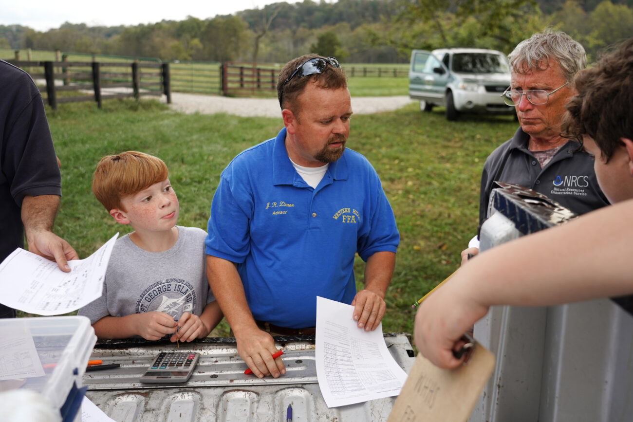J.R. Dinner (middle) grades some of his students and the opposing teams land plotting competitions scores while his youngest son Preston (left) watches him on Thursday, Oct. 14, 2021, in Frankfort, Ky. Western Hills placed second. Photo by Kaitlyn Skaggs