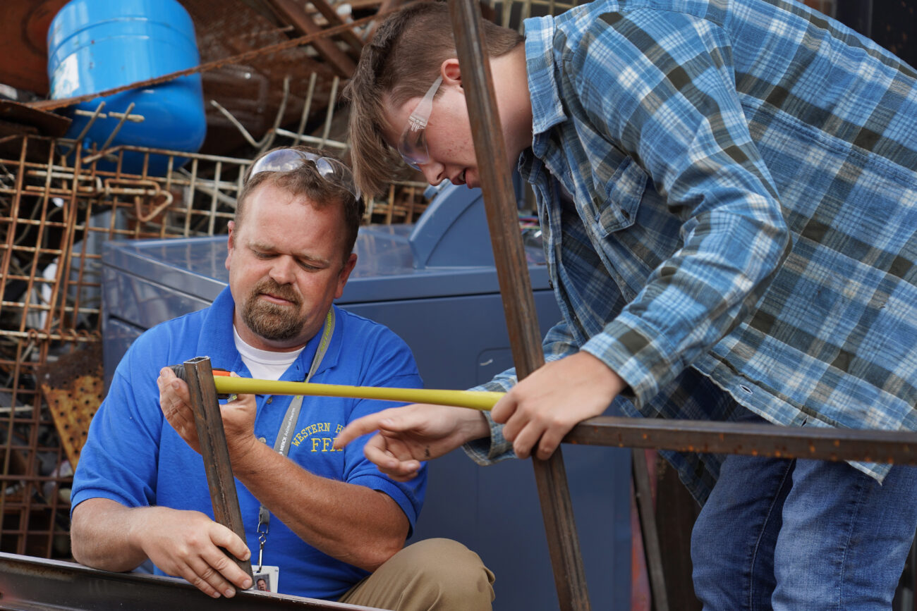 During his agricultural mechanics class J.R. Dinner helps a student measure the space needed between the rods of the canoe trailer the students have been welding and working on on Thursday, Oct. 14, 2021, in Frankfort, Ky. Photo by Kaitlyn Skaggs