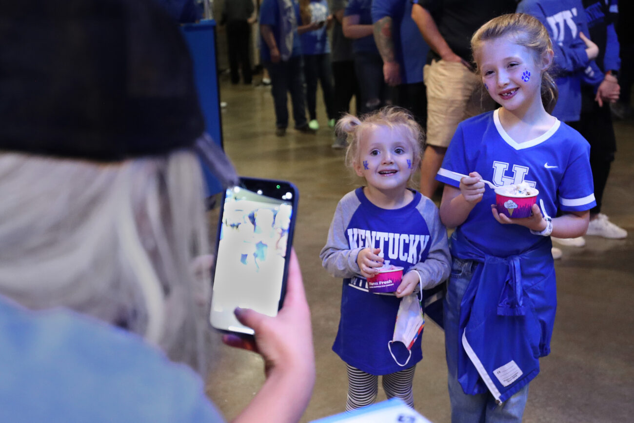 Cook takes a photo for social media of Kate and Claire Adkins (left to right) holding up Taylor Belles ice cream at Rupp Arena during Big Blue Madness.
