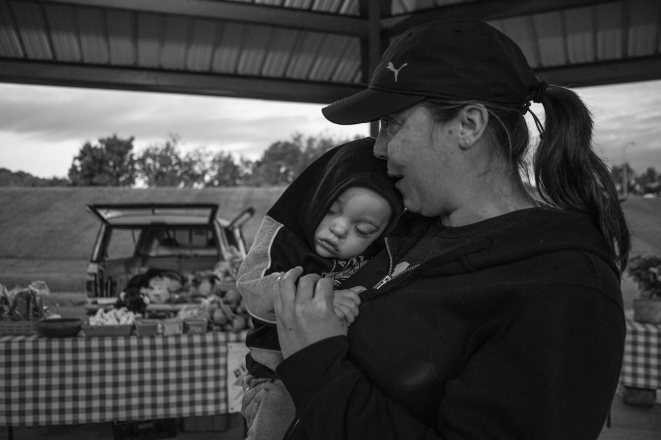 Harrison Buckler, the son of shepherd Emily Buckler, is comforted by his grandmother, Virginia Geddes in Frankfort, Ky. on Saturday, Oct. 16, 2021. They stand by at the Franklin County Farmer’s Market as Emily prepares her booth to sell the meat cuts (Photo by Martha McHaney).