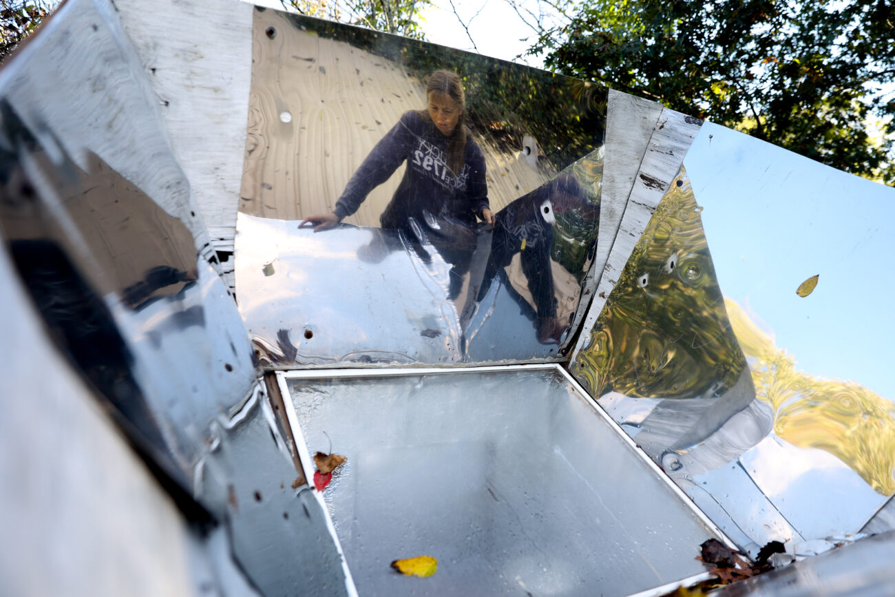 Chris Schimmoeller adjusts her solar oven to face the sun while heating tea on Saturday, Oct. 16, 2021, at her home off of Mount Vernon Road in Frankfort, Kentucky. Reflective material lines the outside of the solar oven to reflect sunlight towards the food located under the transparent screen. Photo by Jack Weaver