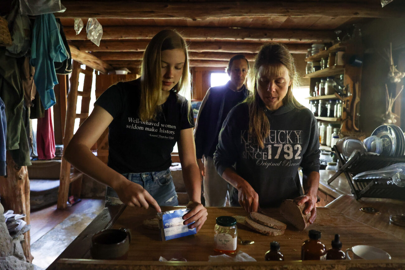 Chris Schimmoeller and her daughter, Sophie Dufour (left), prepare bread with cream cheese and pepper jelly on Saturday, Oct. 16, 2021, at her home off of Mount Vernon Road in Frankfort, Kentucky. The family lives off the electrical grid. The bread was made by Schimmoeller’s brother, Mark. Photo by Jack Weaver