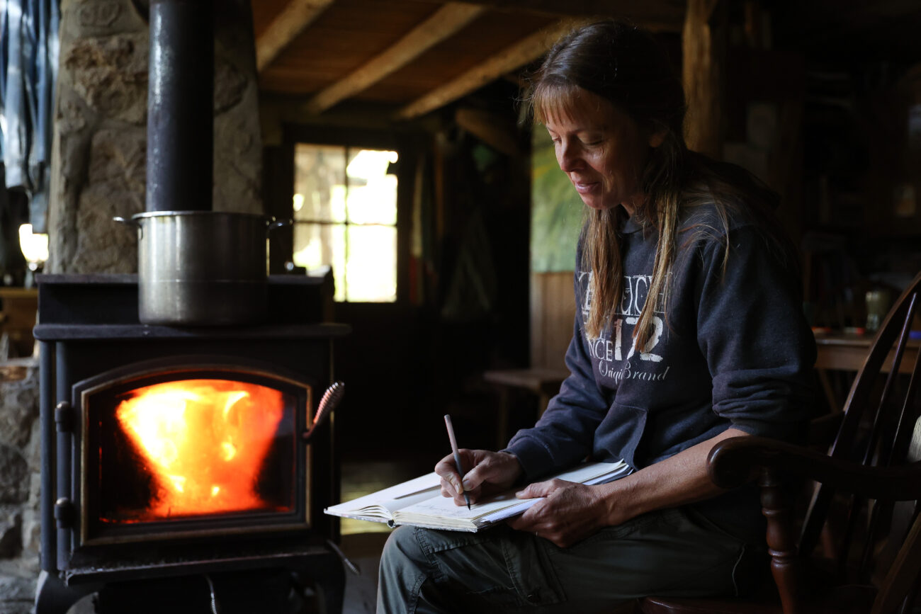 Chris Schimmoeller writes in her family’s woods journal, which is used to take note of everything from daily life to monumental moments on Saturday, Oct. 16, 2021, at her home off of Mount Vernon Road in Frankfort, Kentucky. The family has had a version of the woods journal since they moved to the property in 1991. Photo by Jack Weaver