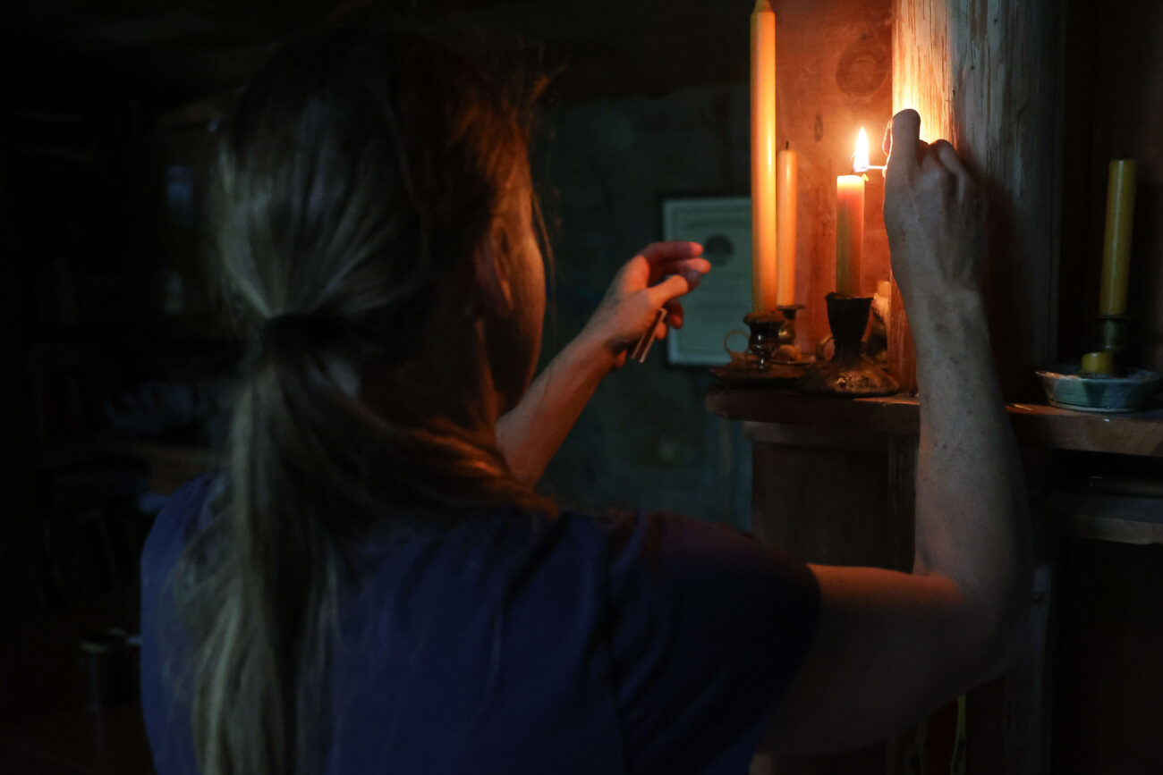 Chris Schimmoeller lights a candle in response to the sun being shaded by clouds on Friday, Oct. 15, 2021, at her home off of Mount Vernon Road in Frankfort, Kentucky. Schimmoeller and her family live off the grid without electricity or running water. Photo by Jack Weaver