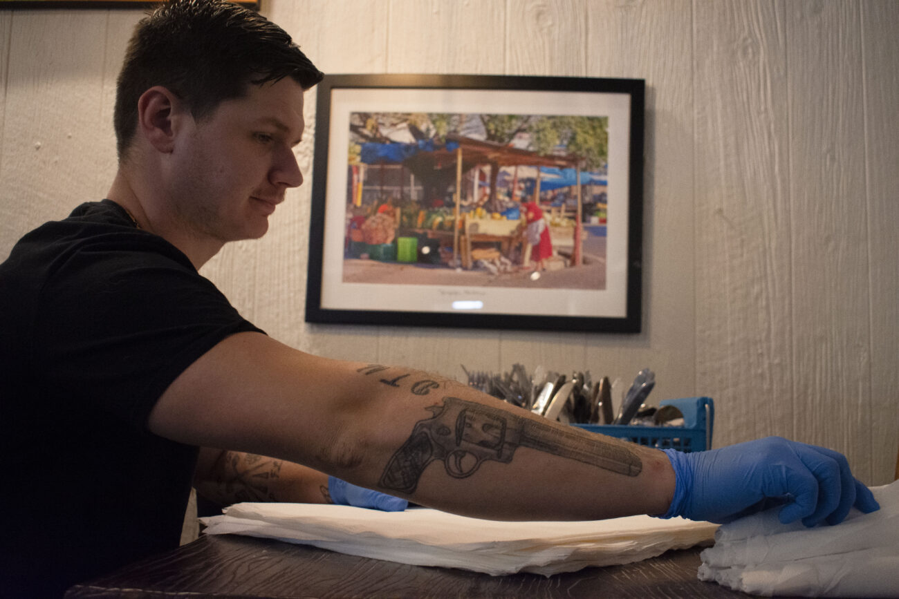 Frank Lang, a server at Mami Monchita’s Honduran restaurant in Frankfort, Kentucky, sits in a booth and folds napkins around silverware before the restaurant fills with customers on Friday, October 8, 2022. Photo | Nyah Leveretter
